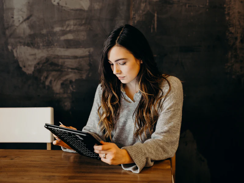 A teacher marking something off on a tablet at a wooden table.